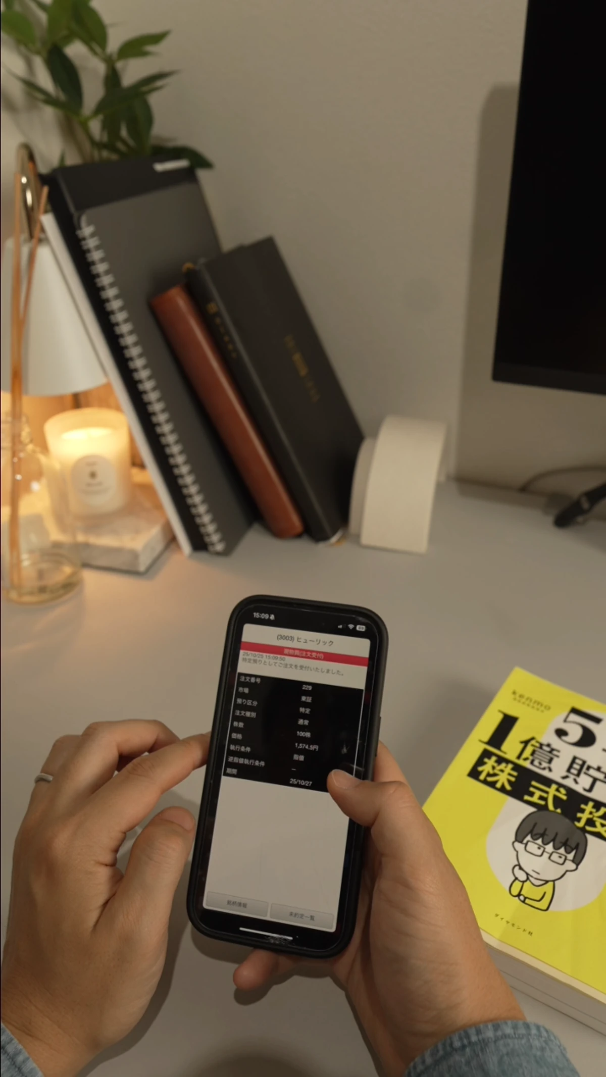自宅のデスクでスマートフォンの株式情報を確認する手元